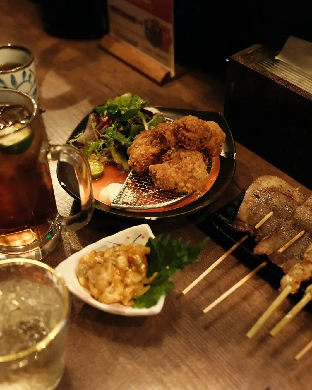 A shared izakaya table set with several dishes under warm low light