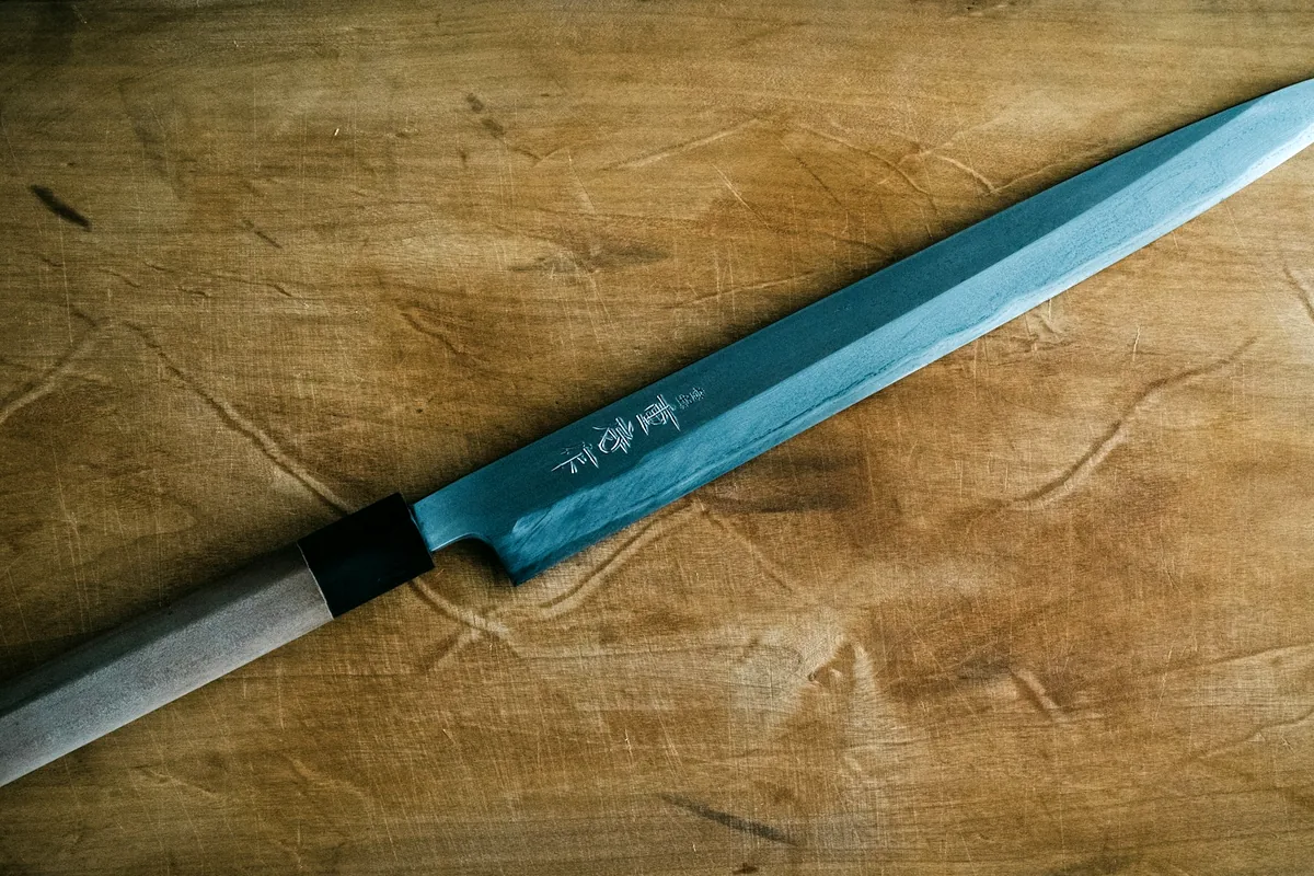 A long single-bevel Japanese knife resting on a wooden board