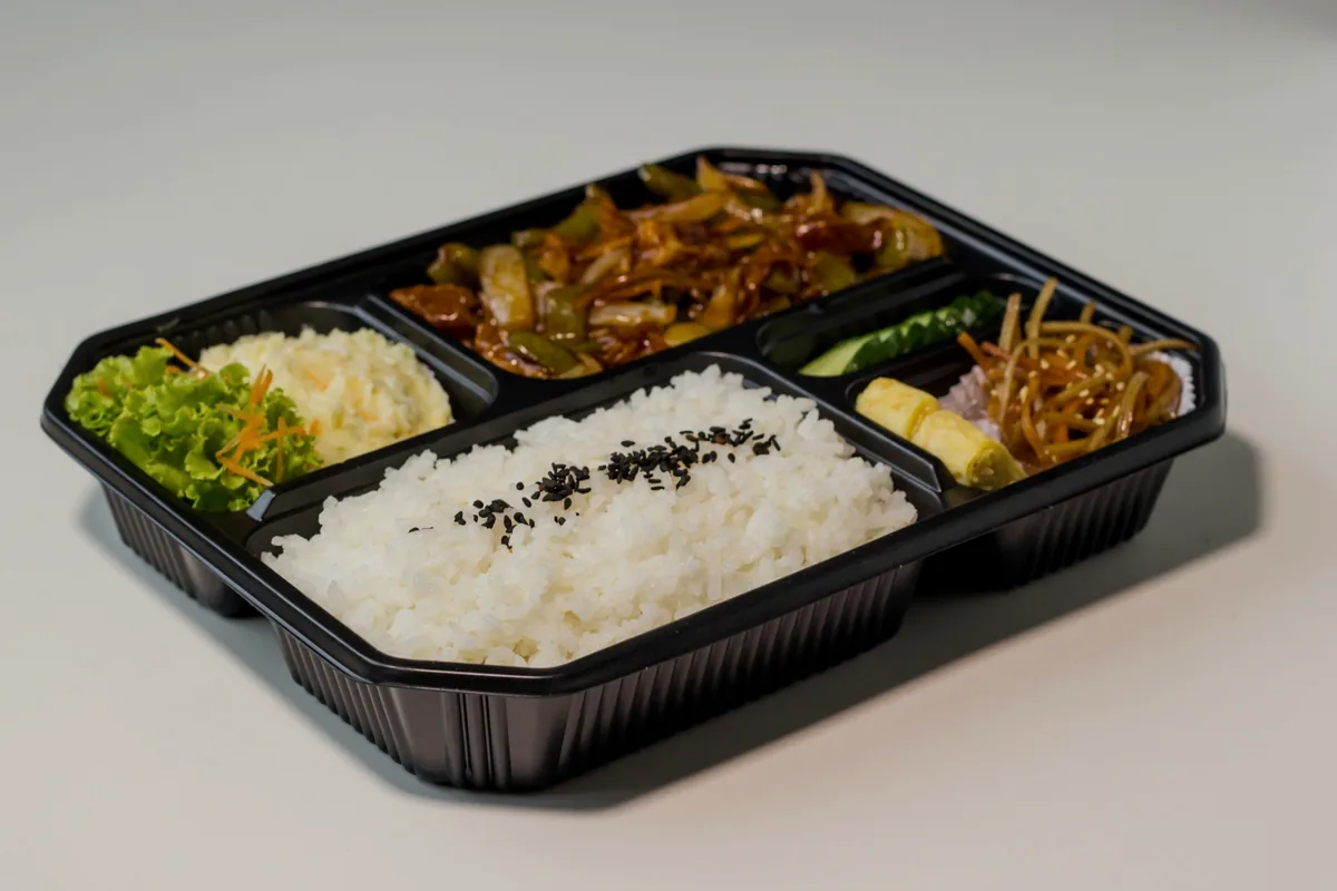 A divided black takeout tray holding rice, salad and a hot dish