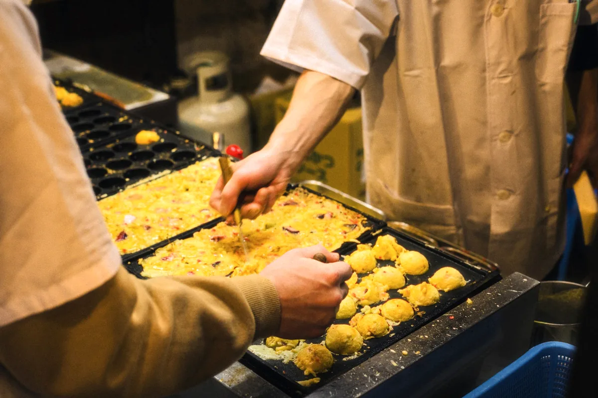 A cook turning batter balls in a moulded cast-iron takoyaki pan