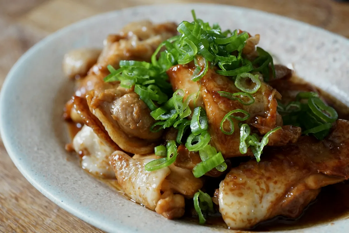 Pieces of chicken coated in a glossy dark glaze and scattered with green onion
