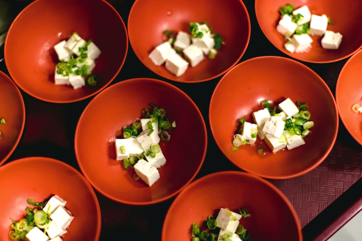 Small red bowls each holding cubes of tofu and chopped herbs