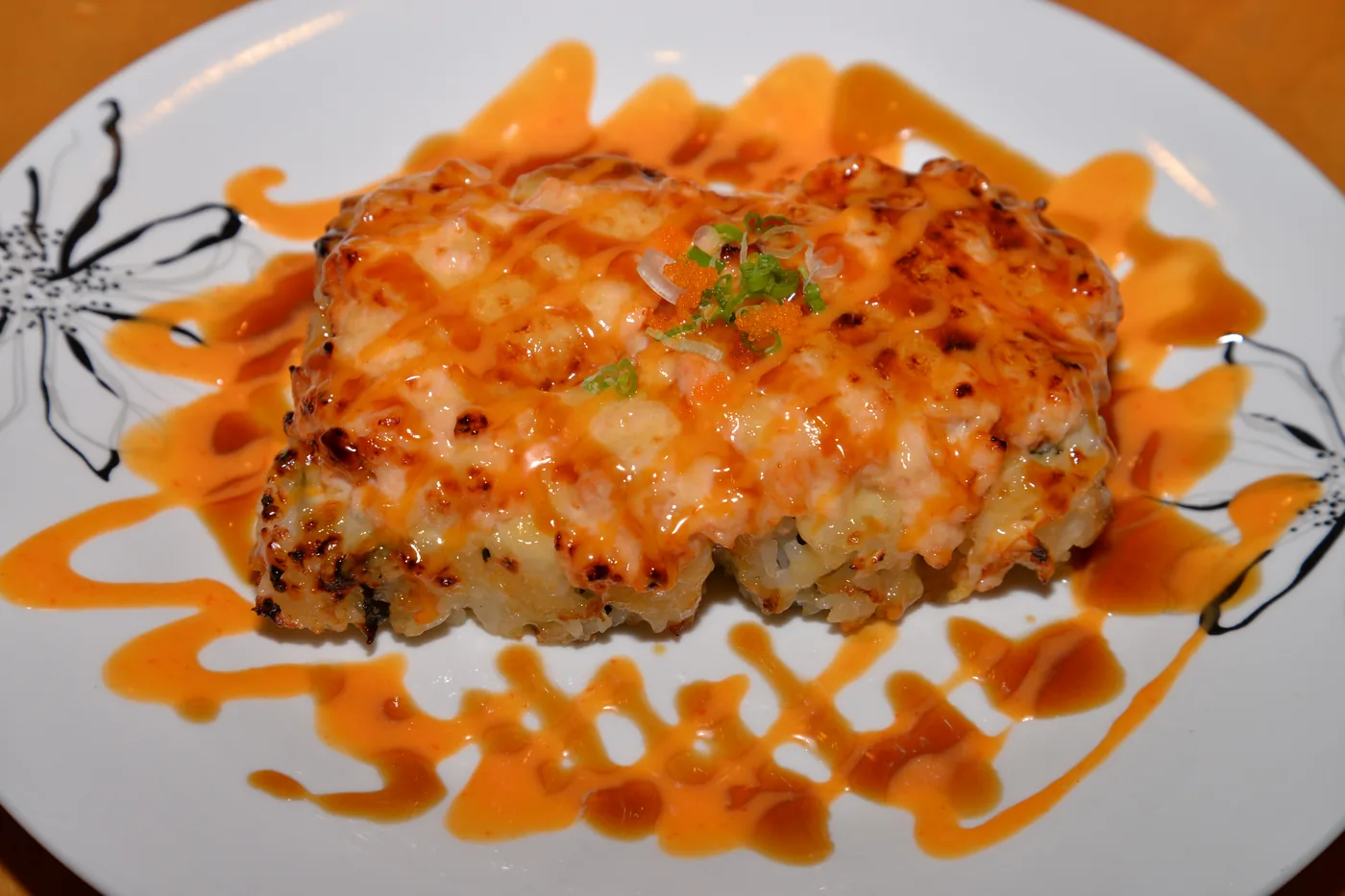 Baked Salmon roll with a browned salmon topping and eel sauce on a white plate