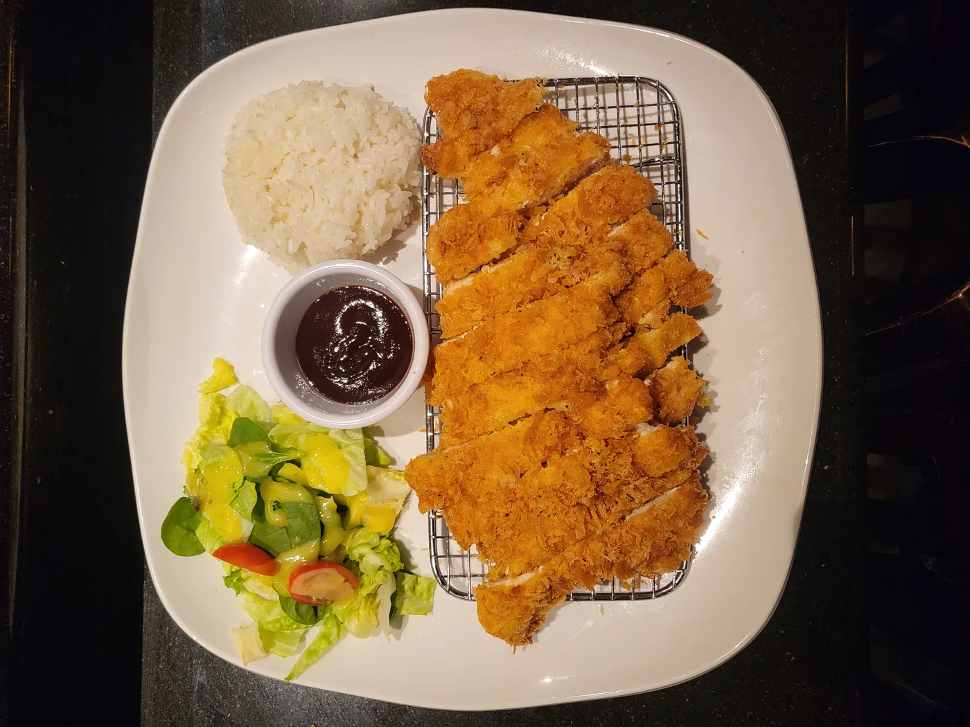 Chicken Katsu, a breaded cutlet sliced on a plate with rice and salad