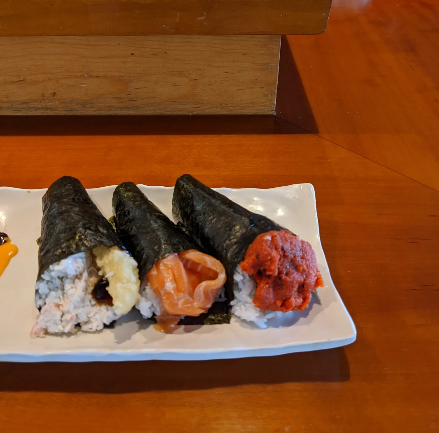 Three hand rolls standing upright on a plate, each wrapped in a seaweed cone