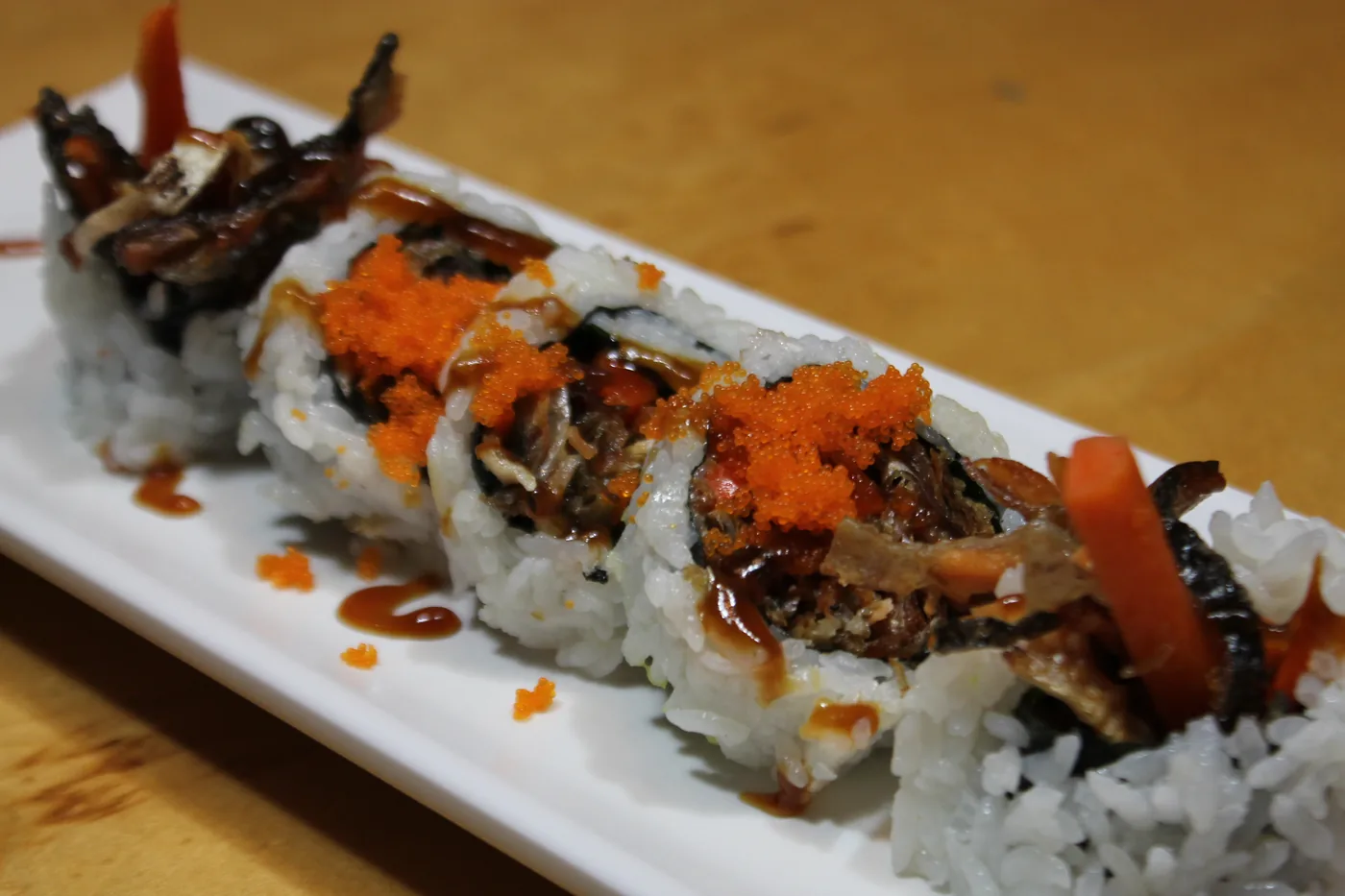 Salmon Skin Roll topped with sauce and roe on a long white plate