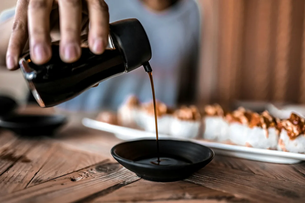 A thick dark sauce being poured from a bottle into a small dish