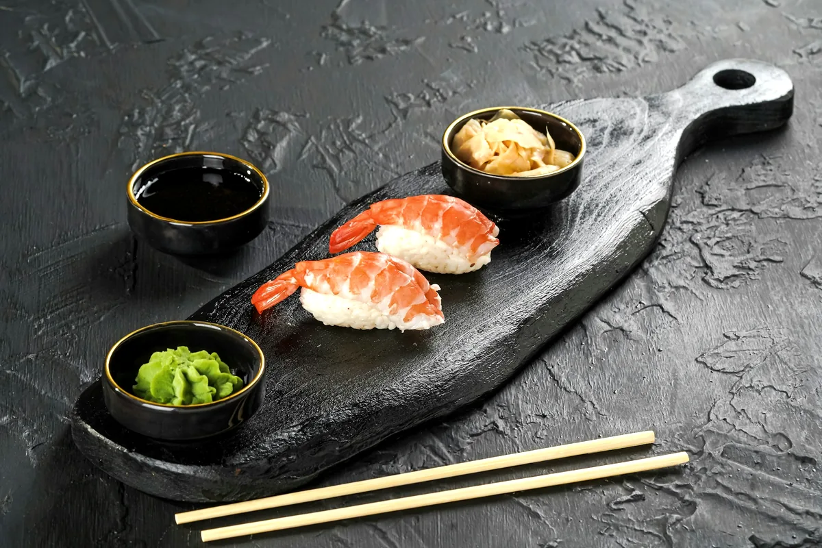 Nigiri on a slate board beside small dishes of wasabi, pickled ginger and soy sauce